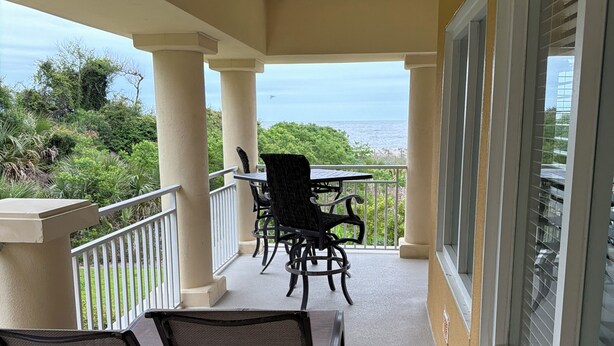 Un balcon avec des chaises et une table, offrant une vue sur un paysage verdoyant et luxuriant et sur l’océan.
