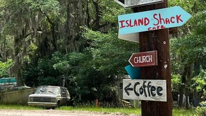 Un panneau indicateur directionnel avec de nombreuses flèches pointant vers différents lieux d’intérêt de la région, tels qu’un musée, une caserne de pompiers et de secours, un parc départemental, une école, un phare, une cabane sur une île, une église et un café.