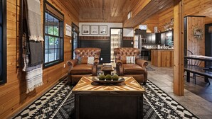 A cozy log cabin interior with leather sofas, a dining table, and a kitchen area.