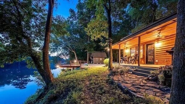 A cabin by a lake with a stone pathway leading to the entrance, surrounded by trees.