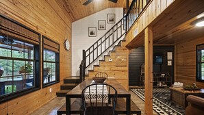 A wooden interior with a dining table, chairs, a staircase, and a view of the outdoors.