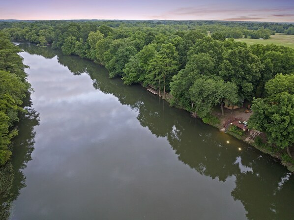 Un río rodeado de bosque denso, con un muelle de madera y zona de estar.