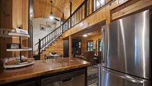 A kitchen with a stainless steel refrigerator, wooden countertops, and a staircase leading to a loft area.