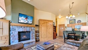 Una sala de estar con chimenea de piedra, sofás de cuero, un televisor y una zona de cocina con armarios de madera.