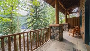 Una terraza de madera con un muro de piedra, sillas de madera y vistas a árboles.