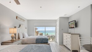 Une chambre avec deux lits, une commode, une télévision et un balcon avec vue sur la mer.