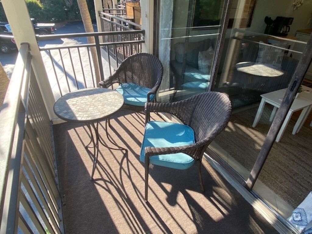 Een balkon met rieten stoelen, een kleine tafel, een glazen deur en uitzicht op de straat.