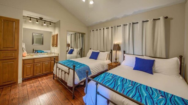 A hotel room with two beds, a bathroom, wooden cabinets, a ceiling fan, and a mirror.
