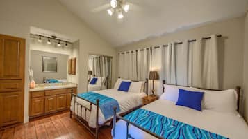 A hotel room with two beds, a bathroom, wooden cabinets, a ceiling fan, and a mirror.