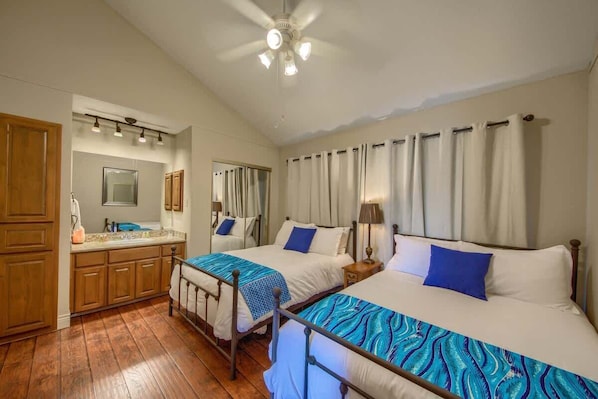 A hotel room with two beds, a bathroom, wooden cabinets, a ceiling fan, and a mirror.