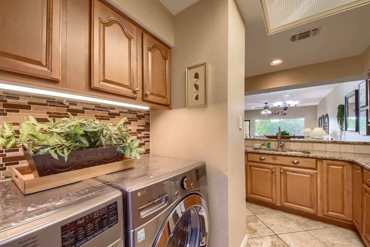 A kitchen with wooden cabinets, a brick backsplash, a washing machine, and a countertop with a plant.
