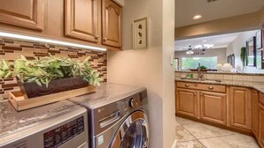 A kitchen with wooden cabinets, a brick backsplash, a washing machine, and a countertop with a plant.