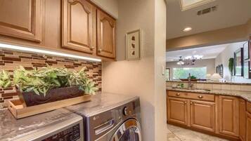 A kitchen with wooden cabinets, a brick backsplash, a washing machine, and a countertop with a plant.