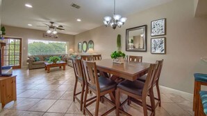 A dining area with a large wooden table, chairs, a chandelier, and artwork on the walls.