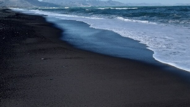 Une plage au sable sombre, bordée par des vagues.