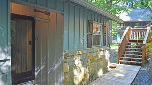 A wooden cabin with a stone wall, a wooden deck, and a staircase leading to a porch.