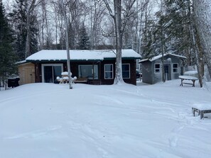 A cabin with a snow-covered roof, a wooden deck, and a small porch area.