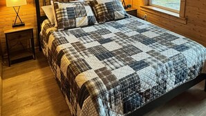 Une chambre dans une cabane en bois, avec un lit, deux tables de chevet, un ventilateur de plafond et une fenêtre donnant sur la forêt.
