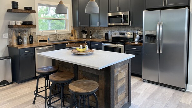 A modern kitchen with dark cabinetry, stainless steel appliances, a central island with stools, and pendant lighting. - Like New Lake & Mountain Views from every room in the house! (Dandridge)