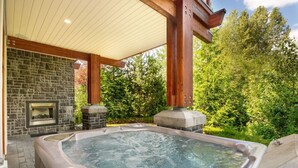 Un jacuzzi bajo una pérgola de madera con paredes de piedra y una chimenea.