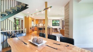Un interior moderno con una mesa de comedor de madera, sillas negras, una escalera y una zona de cocina.