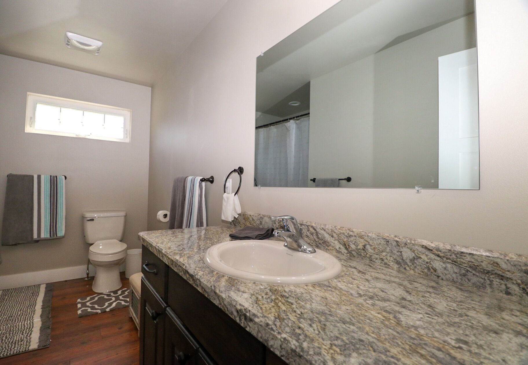 A bathroom with a marble sink, a toilet, a mirror, and a window.