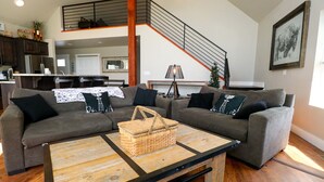 Un salon moderne avec un canapé d’angle gris, une table basse en bois et un escalier menant à un niveau supérieur.