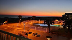 Zwembad van een resort met uitzicht op een zonsondergang, een omheind terras en ligbedden.