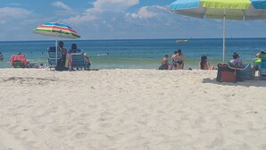 Een strand met twee parasols, een zandstrand en een helderblauwe lucht.