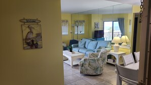 Een woonkamer met een bank, fauteuils en een salontafel. Er hangt een spiegel aan de muur en staat een 'Welcome' bord.