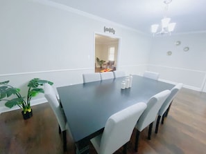 Comedor con mesa de madera oscura, sillas blancas tapizadas, una planta en maceta y un candelabro.