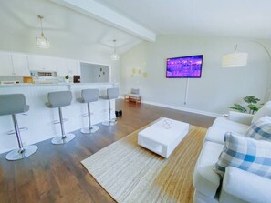 Una sala de estar moderna con un sofá blanco, una mesa de centro y una zona de cocina con taburetes de bar.