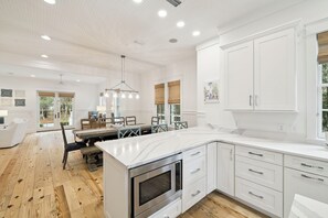 Une cuisine spacieuse avec des meubles blancs, un grand îlot central et un coin repas comprenant une table et des chaises en bois.