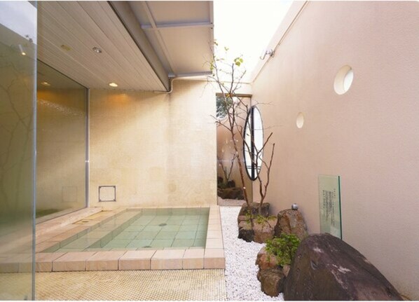 A spa area with a hot tub, a small garden with rocks and a tree, and a glass wall.