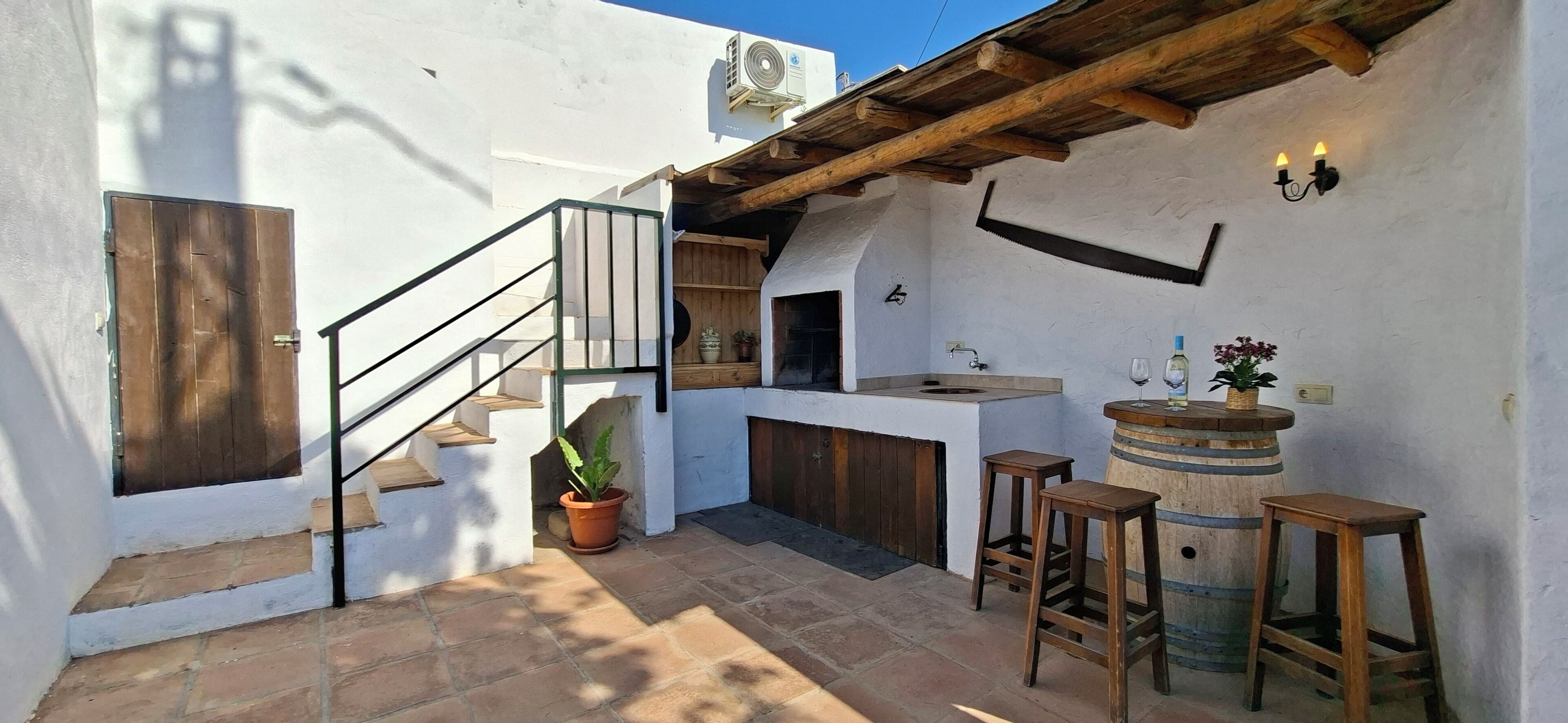 A rustic outdoor kitchen with a wooden staircase, a potted plant, and a barrel.