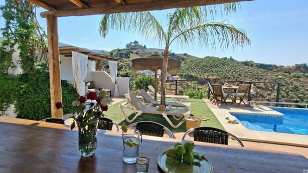 Zona junto a la piscina con sillones de descanso, una mesa con una jarras de agua y limones, y vistas del paisaje circundante.