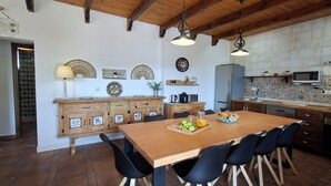 Una cocina con armarios de madera, una mesa de comedor con sillas, un microondas y un reloj en la pared.