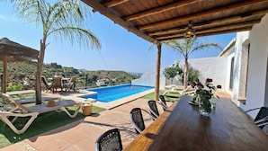 Zona de piscina con sillas de descanso, una mesa de madera y vistas al paisaje.