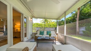 Un patio cubierto con muebles de mimbre, un sofá con cojines y una mesa con un libro.