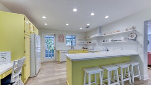 Una cocina moderna con una isla central, taburetes blancos y vistas al exterior a través de un ventanal.