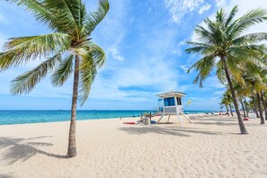 Une plage avec une tour de surveillance, des palmiers et un ciel bleu dégagé.