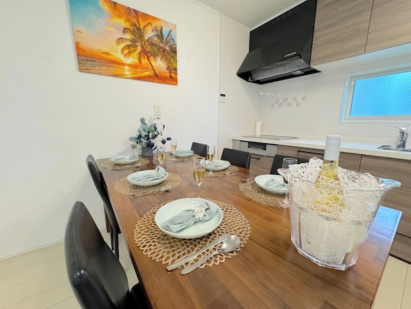 Un coin repas avec une table en bois dressée pour quatre personnes, un vase en verre décoratif et un tableau représentant un coucher de soleil accroché au mur.