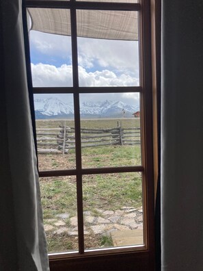 Ein Fenster mit Blick auf eine gebirgige Landschaft, einem Holzzaun und ein Gebäude in der Ferne.