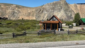 Eine rustikale Holzhütte mit Veranda, umgeben von einem Holzzaun, vor einer Bergkulisse.