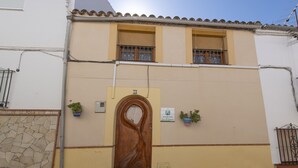 Un bâtiment à deux étages, doté d’une porte en bois, de deux fenêtres avec volets et d’un mur en pierre.