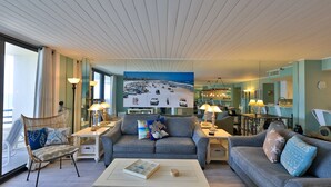 Una sala de estar con un amplio mural de playa, dos sofás, una mesa de centro y un comedor con candelabro.