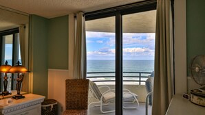 Una habitación con vista al océano, una silla blanca, una lámpara y un reloj.