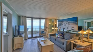 Una habitación con sofá, televisor, mesa y vista al mar.
