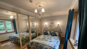 A bedroom with two beds, wooden flooring, a large mirror, and a window with curtains. - Country Cottage Sleeps 6 w/ Hot Tub & Dog-friendly (Thornhill)