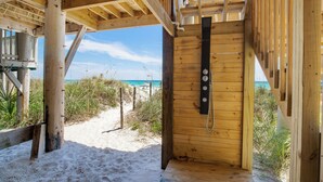 Un abri de plage en bois, équipé d’une douche, avec un chemin de sable et vue sur la plage.
